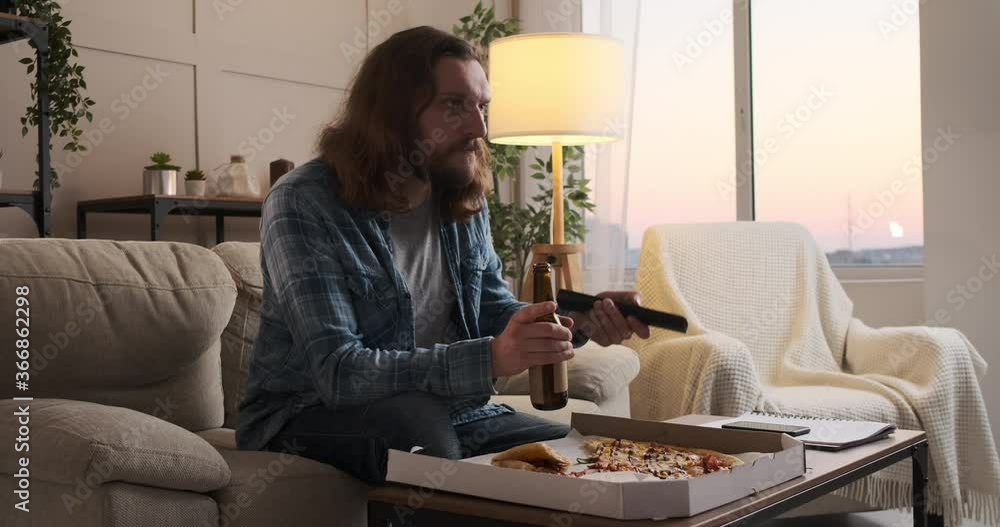 Man eating pizza and drinking beer while watching tv at home Man eating pizza and drinking beer while watching tv at home