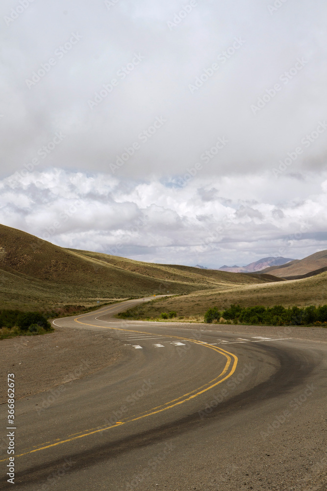 Countryside road. Asphalt highway curve across the golden meadow in autumn. The yellow grassland and hills under a cloudy sky. Countryside road. Asphalt highway curve across the golden meadow in autumn. The yellow grassland and hills under a cloudy sky.