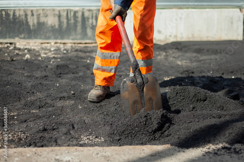A worker with a shovel is laying asphalt.