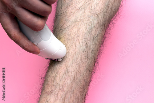 Obraz na plátne Man epilates his leg with an electric epilator device