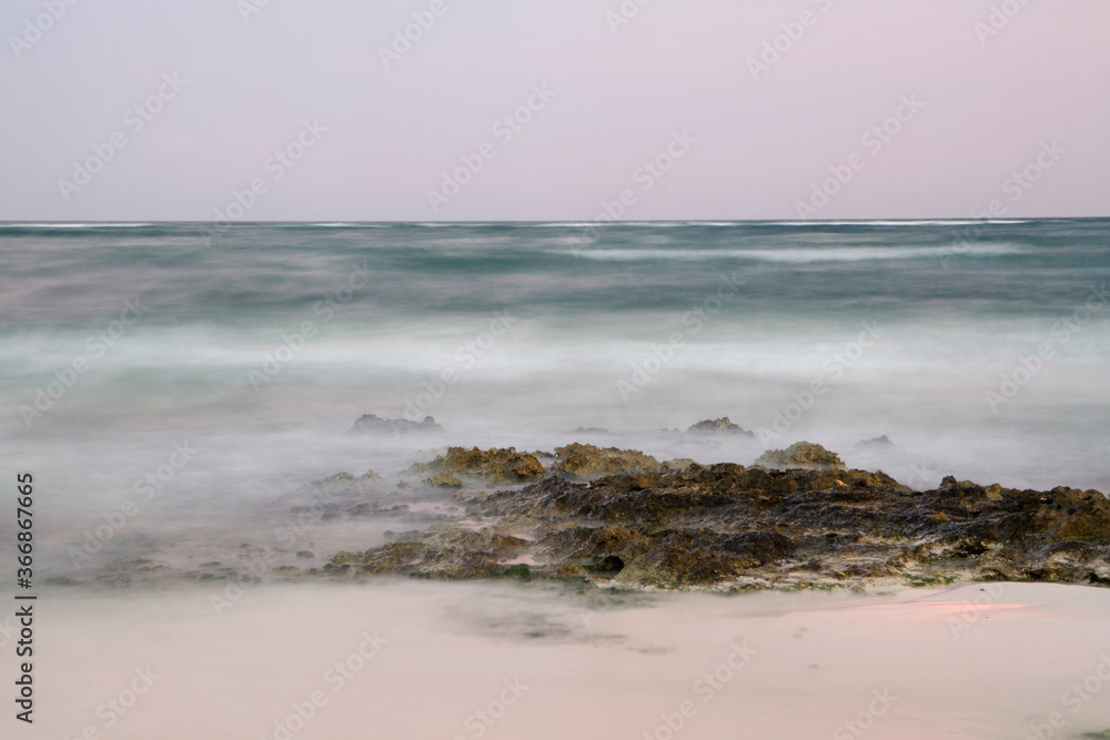 Long exposure shot of the ocean water and shore at sunset. Dreamy view of the blurred sea waves and rocks with magical twilight colors.