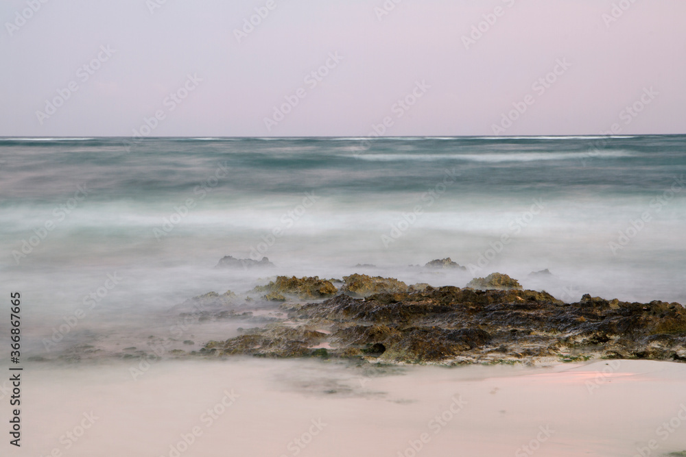 Long exposure shot of the ocean water and shore at sunset. Dreamy view of the blurred sea waves and rocks with magical twilight colors. Long exposure shot of the ocean water and shore at sunset. Dreamy view of the blurred sea waves and rocks with magical twilight colors.