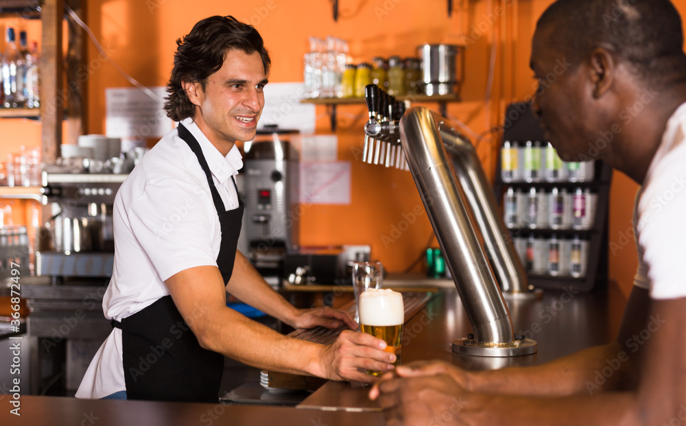 Young man barman giving beer with foam to man client in bar