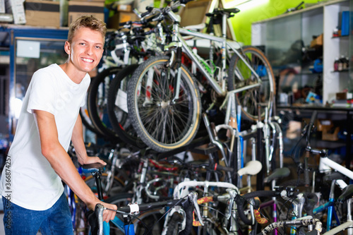 Positive cheerful young male standing near the cycle in the shop