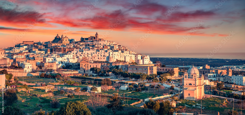 Panoramic evening cityscape of Ostuni town. Majestic summer sunset on Apulia, Italy, Europe. Traveling concept background. Beautiful world of mediterranean countries..