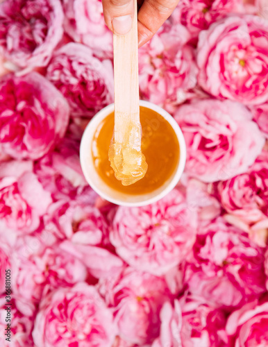 depilation and beauty concept - sugar paste or wax honey for hair removing with wooden waxing spatula sticks on flower background. copyspase.