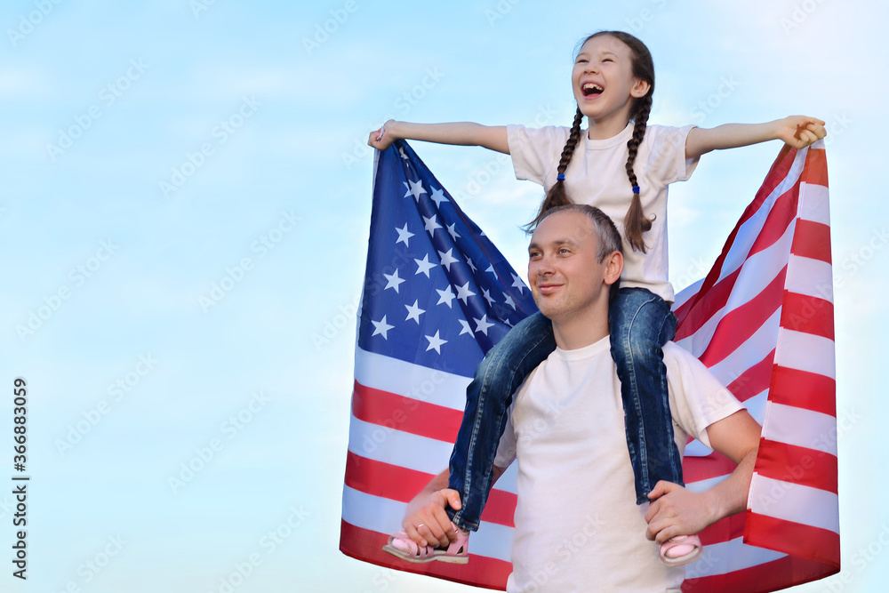 Fototapeta premium Happy daughter sits on her father's shoulders and holds the American flag above her head. American Independence Day. Happy future concept. Freedom. Election.Copy space for text.
