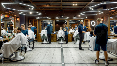 People at barbershop. Professional barbers serving clients in the modern loft style barber shop. General view. Hairdresser services