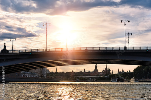 Historic moscow city skyline kremlin landmark at sunset on summer evening against backlit sun background. Urban street view of people crossing Moskva river by Moscow Bolshoi Ustyinskiy bridge
