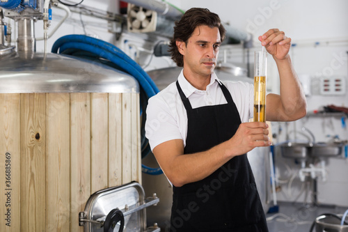 Worried man expert is standing with flask for beer and analizying quality in beer factory