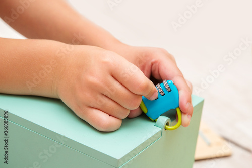 
Close-up of children's hands holding a lock with a code to guess the code on the lock and open the box