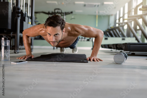 Muscular build man doing push-ups in a gym.