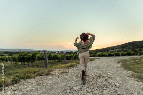 Girl in a cowboy hat at sunset in the countryside in the vineyards.