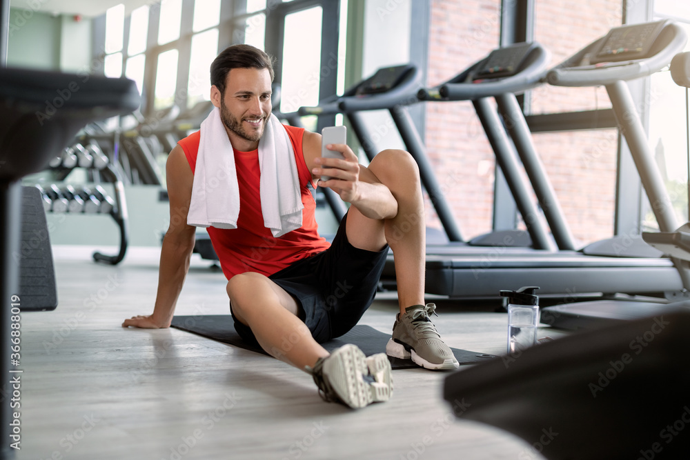 Happy athletic man text messaging on cell phone in health club.