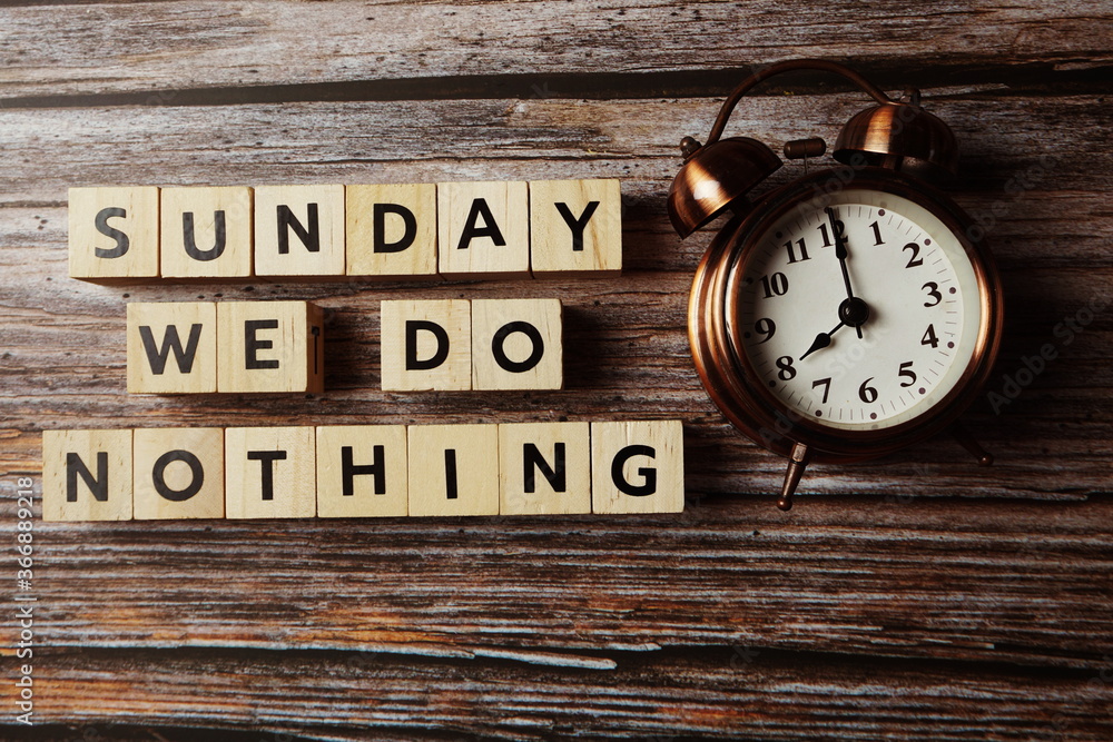 Sunday We do nothing alphabet letter with alarm clock on wooden background; Sunday We do nothing alphabet letter with alarm clock on wooden background;