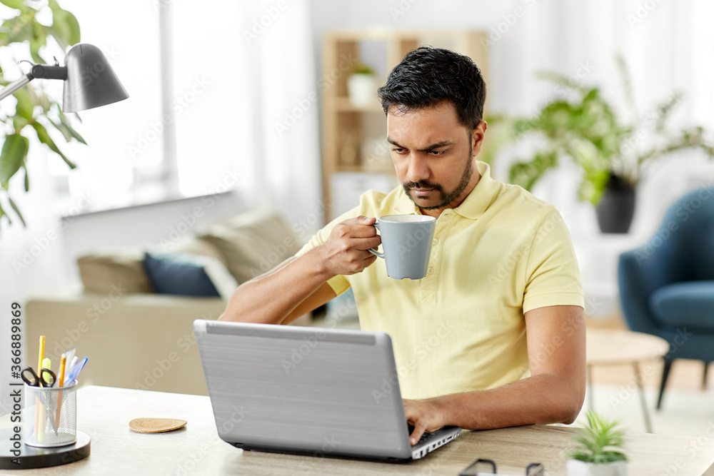 technology, remote job and lifestyle concept - indian man with laptop computer drinking coffee or tea at home office technology, remote job and lifestyle concept - indian man with laptop computer drinking coffee or tea at home office