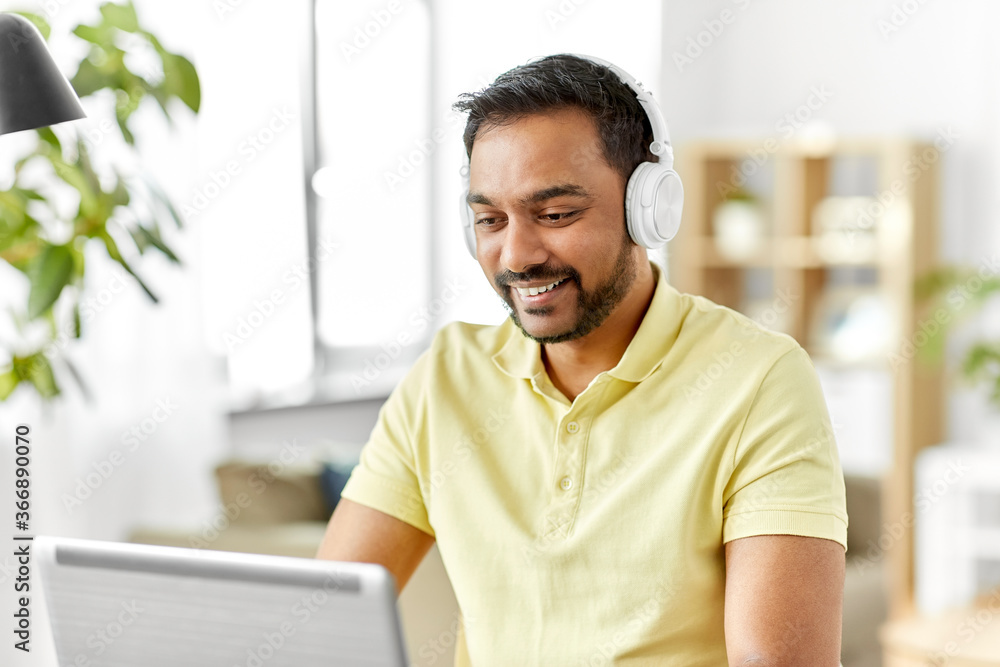 remote job, technology and people concept - happy smiling young indian man in headphones with laptop computer working at home office remote job, technology and people concept - happy smiling young indian man in headphones with laptop computer working at home office