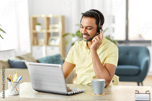 remote job, technology and people concept - happy smiling indian man with headset and laptop computer having conference call at home office