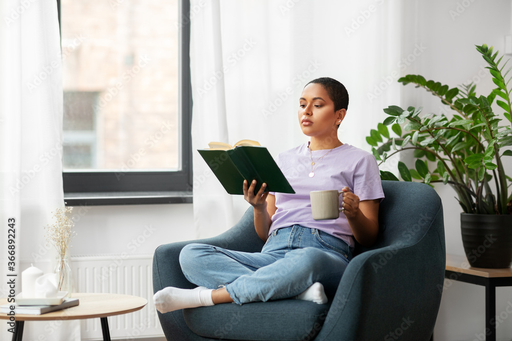 people and leisure concept - african american woman in glasses sitting on sofa and reading book at home people and leisure concept - african american woman in glasses sitting on sofa and reading book at home