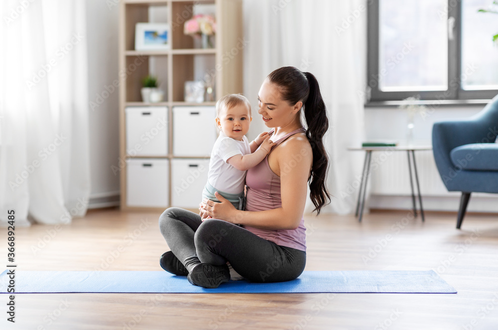 family, sport and motherhood concept - happy smiling mother with little baby sitting on exercise mat at home family, sport and motherhood concept - happy smiling mother with little baby sitting on exercise mat at home