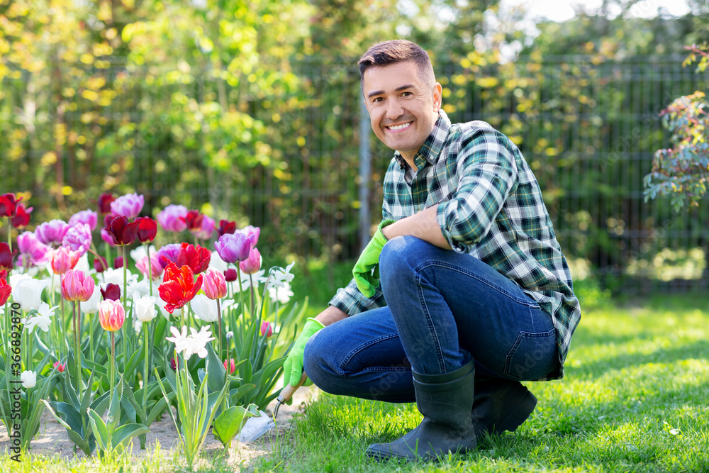 gardening and people concept - happy smiling middle-aged man with scoop taking care of flowers at summer garden gardening and people concept - happy smiling middle-aged man with scoop taking care of flowers at summer garden