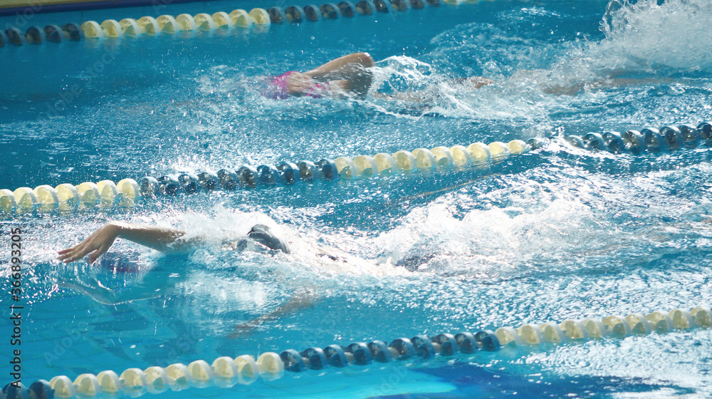 Two young athletes swim on their backs in the competition pool, body under water, wave of the hand, splashing water.