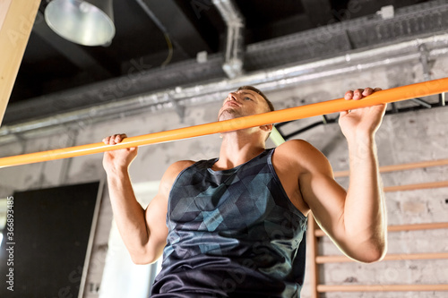 sport, fitness, exercising and people concept - man doing pull-ups on horizontal bar in gym