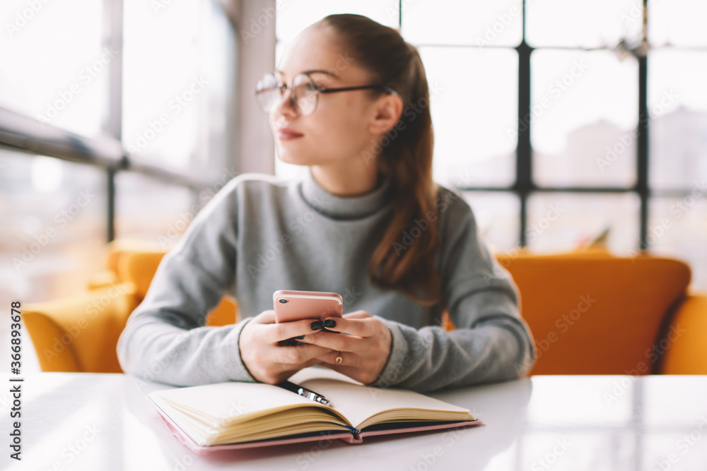 Obraz premium Selective focus on modern smartphone in hand of female student chatting with friends in networks and dreaming about weekend.Blurred businesswoman looking away in window downloading files on mobile