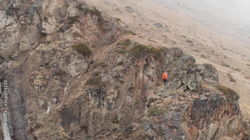 An aerial view of a young photographer with a DSLR camera in his hand stands high on a rock against a waterfall in a snowfall. Extreme landscape photographers in nature An aerial view of a young photographer with a DSLR camera in his hand stands high on a rock against a waterfall in a snowfall. Extreme landscape photographers in nature