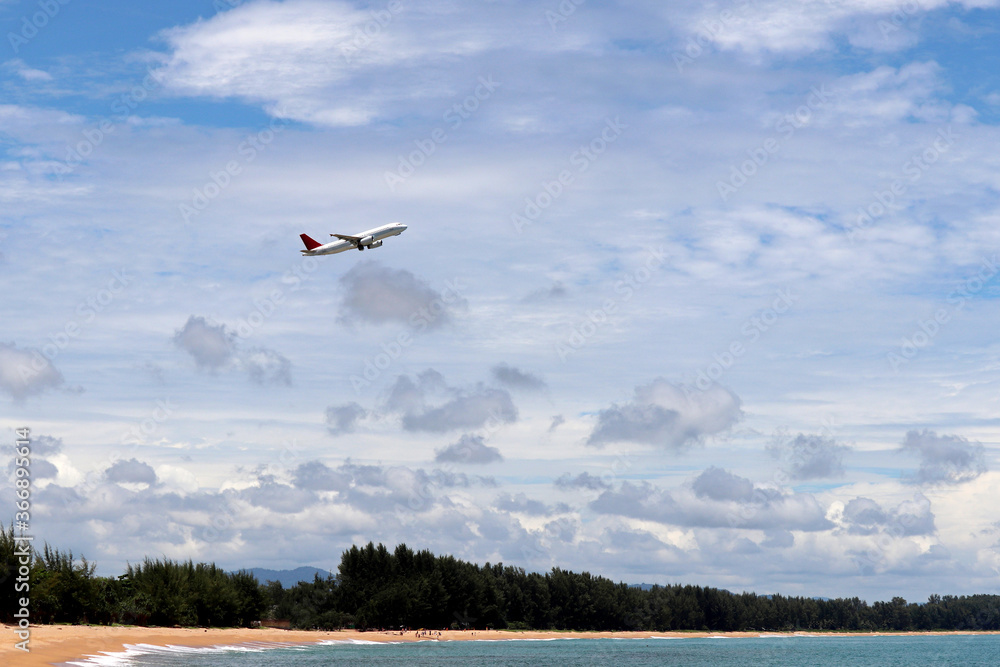 Airplane flies over the sea and tropical beach covered by green forest. Aircraft during taking off on background of blue sky and white clouds, summer vacation and travel concept Airplane flies over the sea and tropical beach covered by green forest. Aircraft during taking off on background of blue sky and white clouds, summer vacation and travel concept