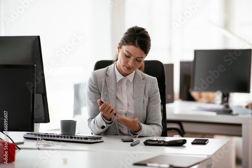 Beautiful businesswoman using lancet pen in office. Young woman checking blood sugar level  © JustLife