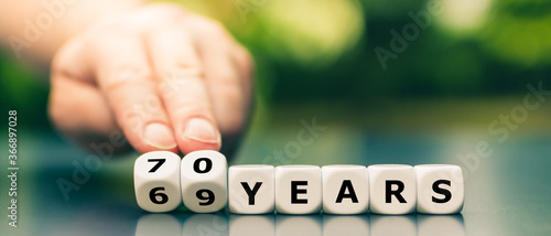 Hand turns dice and changes the expression "69 years" to "70 years".