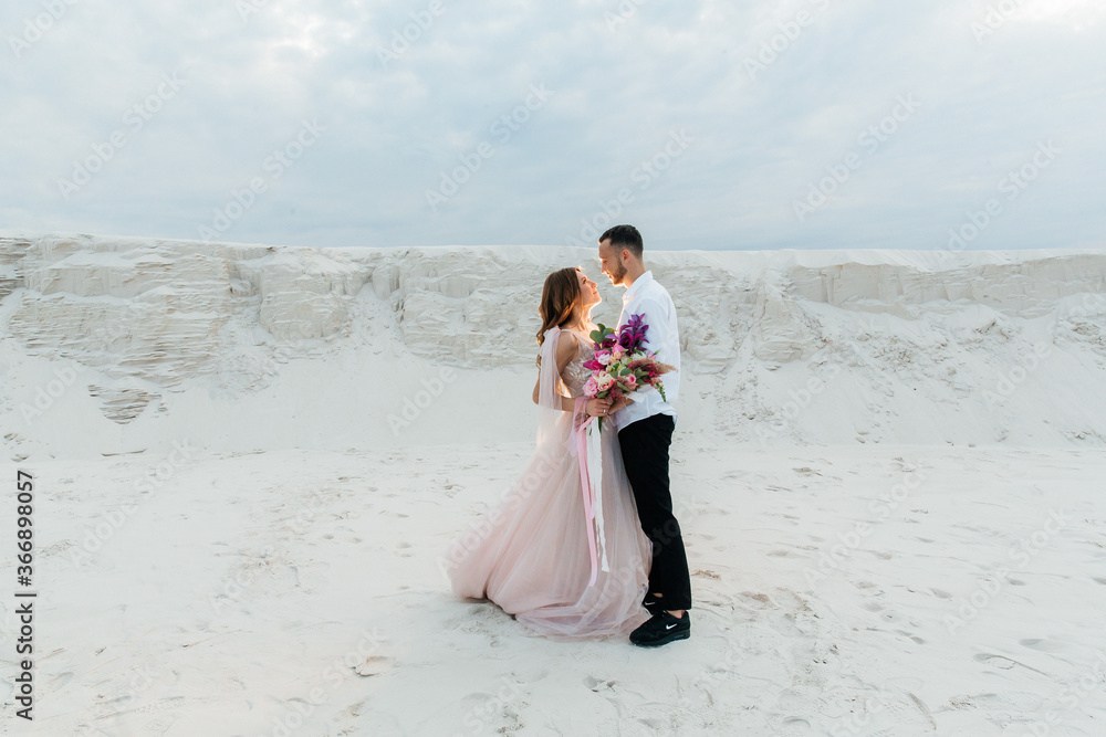 Love Story of a beautiful couple in a pink wedding luxury dress with a bouquet in the Sahara desert, sand, dunes