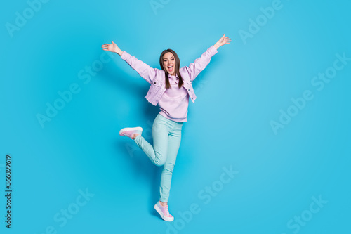 Full length photo of crazy funny lady raise hands leg up students party good mood meet friends wait hugs wear casual denim violet jacket pullover pants shoes isolated blue color background