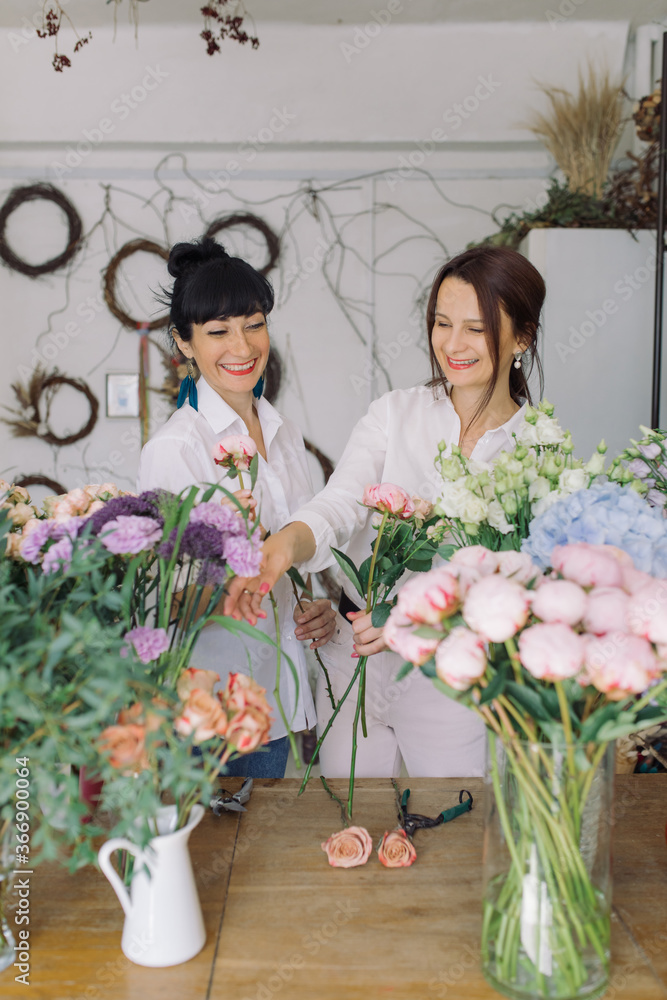 Smiling female florists working at a table in their flower shop arranging bouquets. Small floral business owner. Female power startup concept.