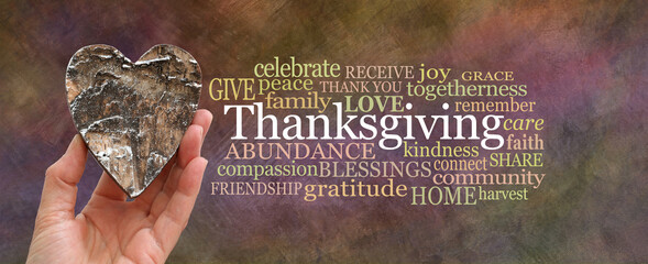 Put some love into Thanksgiving Word Cloud concept - hand holding a rustic brown wooden heart beside a THANKSGIVING word cloud on oil painted warm coloured background
