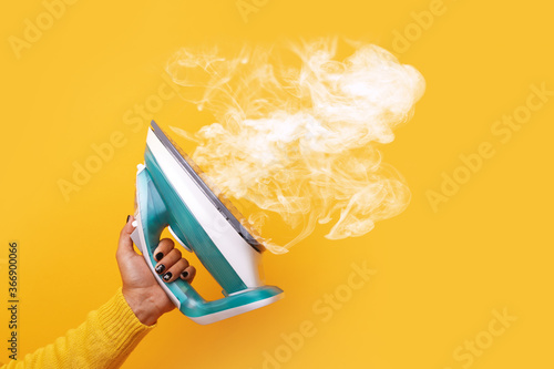 Foto modern iron with steam in hand over yellow background