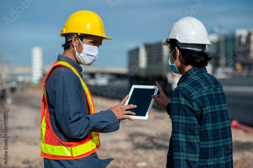 Two engineer talking project construction on site,Man two people a wearing face mask working meeting on tablet at site work place