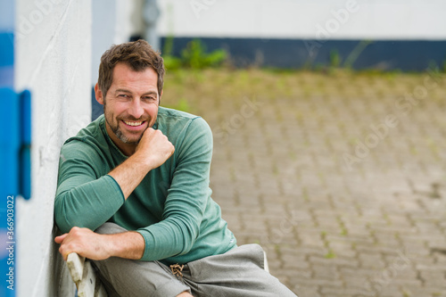 Foto Mann sitzt entspannt auf einer Bank, und sieht positiv nach vorne,im Hintergrund
