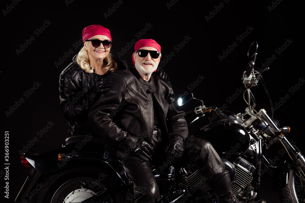 Photo of two aged bikers grey hair man lady couple sit vintage chopper moto feel young rock festival photographing wear trendy rocker leather jacket pants isolated black color background