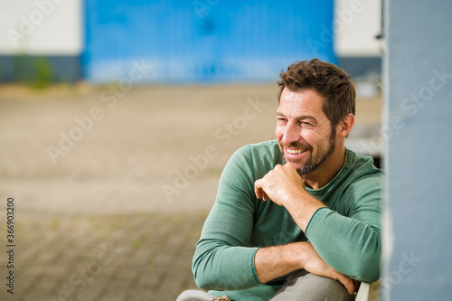 Mann sitzt entspannt auf einer Bank, und sieht positiv nach vorne,im Hintergrund ist viel Platz für Text 