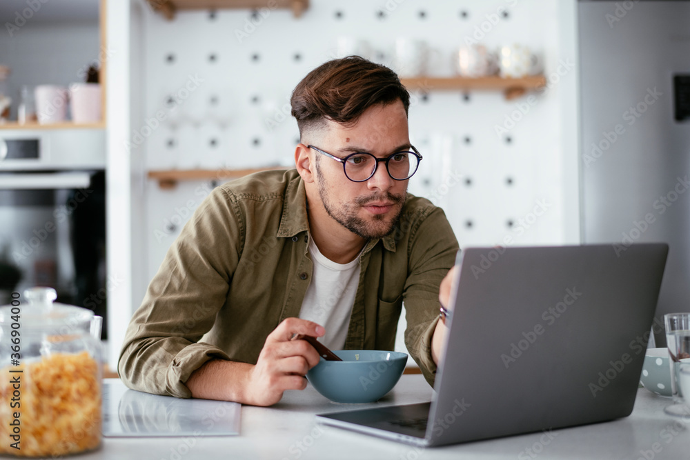 Young man eating breakfast and reading the news online. Handsome man enjoying at home.
Young man eating breakfast and reading the news online. Handsome man enjoying at home.