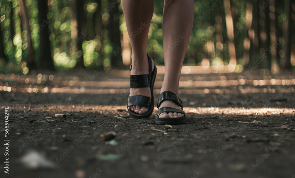 a girl walks through the forest alone, female legs close-up. Young girl in sandals a girl walks through the forest alone, female legs close-up. Young girl in sandals