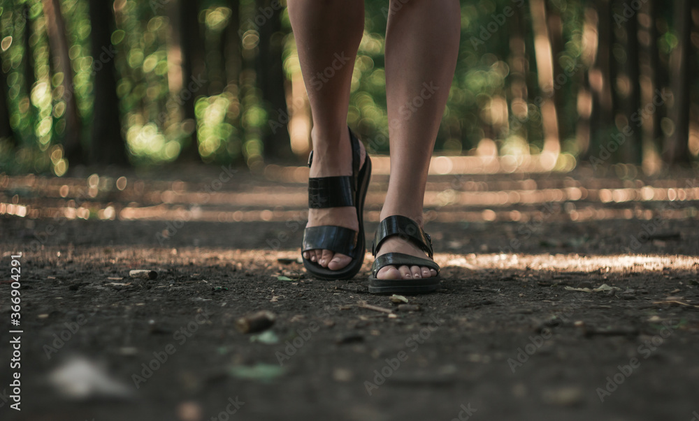 a girl walks through the forest alone, female legs close-up. Young girl in sandals