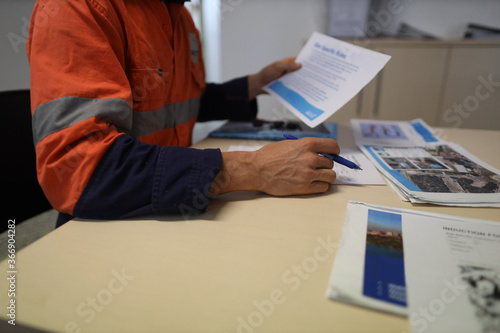 Safety workplace construction worker setting on a chair holding a pen while reading site safety induction rule and regulation evacuation plan prior first time working on site photo