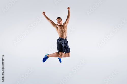Full size photo of handsome sportsman dark skin guy naked chest jump high up celebrate competition winning raise arms up wear shorts sneakers isolated white color background
