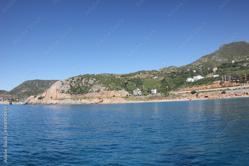 Alanya, TURKEY - August 10, 2013: Travel to Turkey. The waves of the Mediterranean Sea. Water surface. Mountains and hills on the coast of Turkey. Green hills. Port.