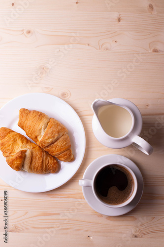 a white ceramic cup with black espresso  french croissant as breakfast or snack concept on rustic  natural texture wooden surface