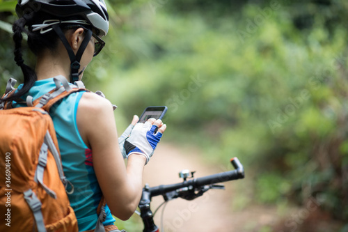 Cyclist use smartphone when riding mountain bike on forest trail.