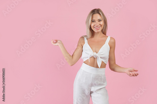 Young blonde woman in white natural flax look and green heels on pink background
